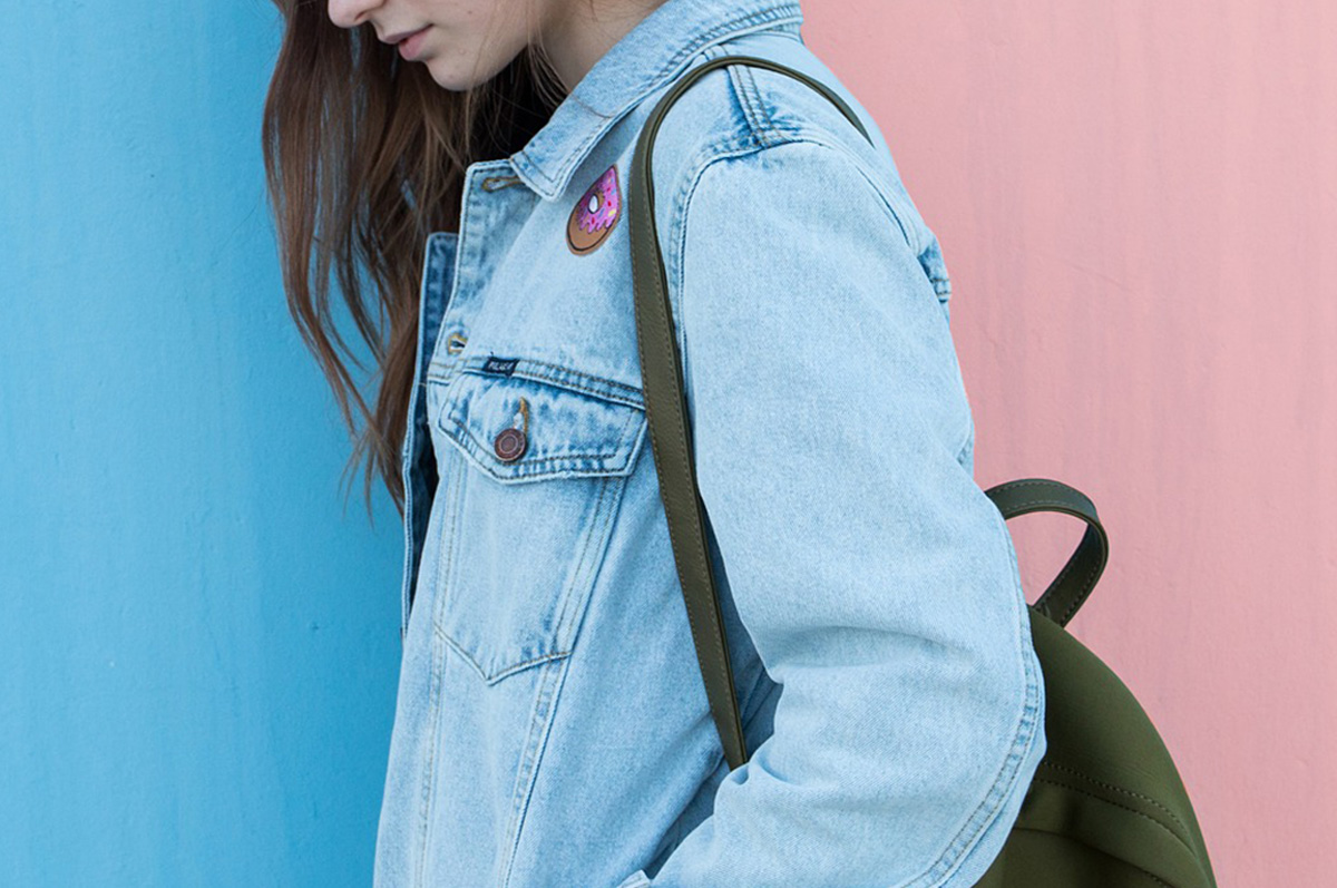 Image of a young woman wearing a jeans jacket walking to the left, carrying a backpack