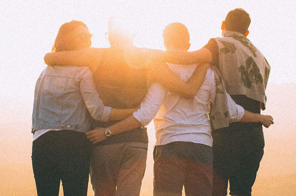 Group of 4 similar aged people watching a sunrise, with arms around each other